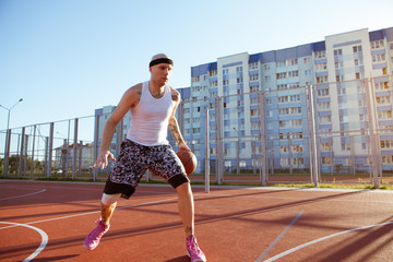 Obraz premium Guy plays basketball on a red Court in sunny weather the background of houses. Solar flare in the frame.