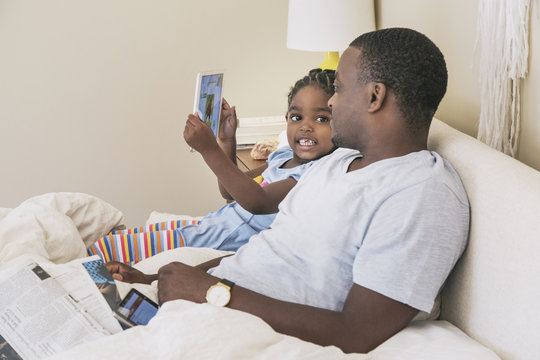 African American father and daughter using digital tablet on bed - Powered by Adobe