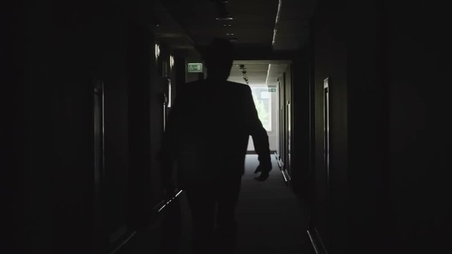 Rear view of silhouette of office worker holding briefcase while running through dark corridor in slow motion