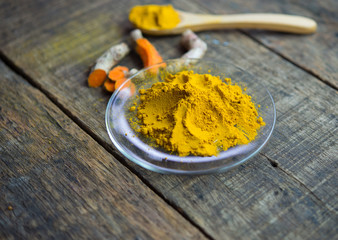 Turmeric powder and fresh roots on wooden table.