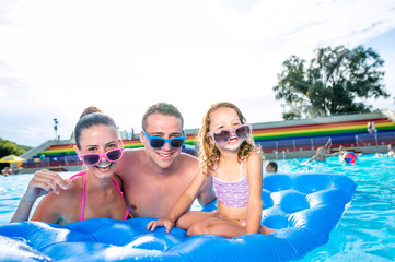 Mother, father and daughter in swimming pool. Sunny summer.