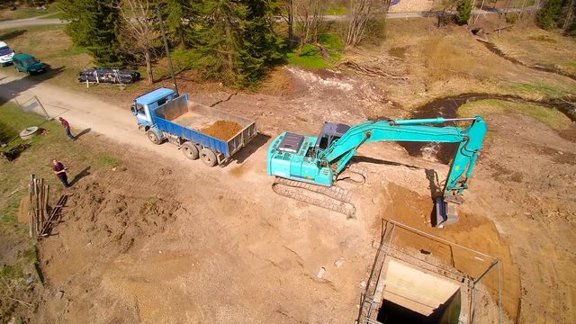 The 360 degrees aerial view of the backhoe and the forest. THe blue backhoe digging a deep hole and transferring the soil on the big dumptruck