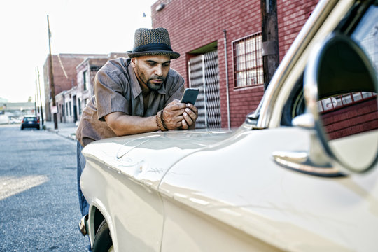 Hispanic Man Using Cell Phone On Vintage Car