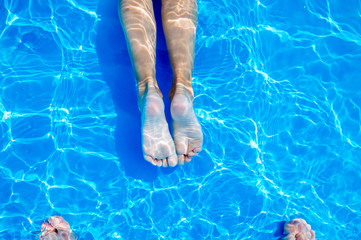 Young womans legs in swimming pool. Summer heat.
