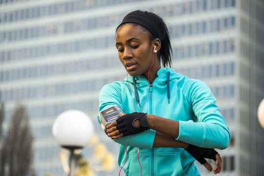 Black runner using cell phone near high rise buildings
