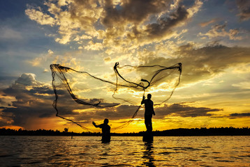 Silhouette  fisherman casting a nets into the water during sunset.