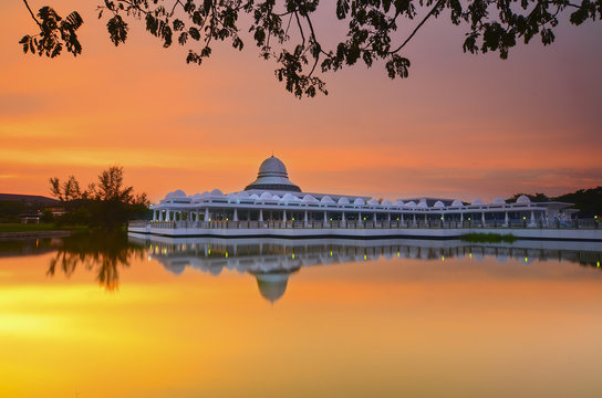 Beautiful white mosque during burning sunrise with mirror reflection on the lake
