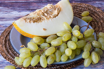  Melon and grapes   A piece of melon and a bunch of ripe grapes on a metal plate on old wooden table.