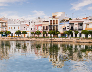 Fototapeta premium Traditional white architecture of the region along the riverbank in Ayamonte, Huelva province, Andalucia, Spain. The buildings and clouds are reflecting in the river.