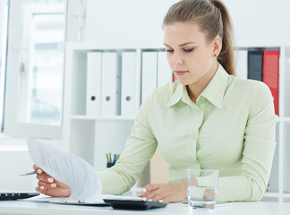 Beautiful young secretary .viewing entries in the papers on the clipboard sitting at office. 