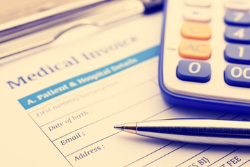 Vintage / retro color style : Blue ballpoint pen, a calculator and a medical invoice on a clipboard.