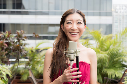 Asian vocalist happily smiling and singing with mic on rooftop of the building