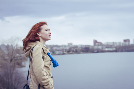 Beautiful young woman with red hair standing near the lake