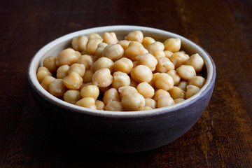 Cooked chickpeas in brown ceramic bowl isolated on dark.