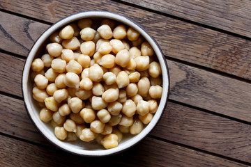Cooked chickpeas in brown ceramic bowl isolated on dark from above.