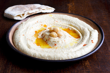 Hummus in brown ceramic bowl with pita bread isolated on dark.
