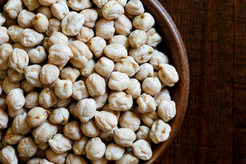 Detail of dried chickpeas in brown wooden bowl on dark from above.