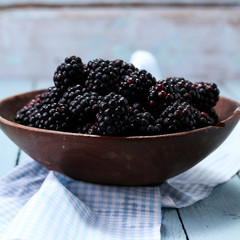 Ripe blackberries in a ceramic bowl on burlap cloth over wooden background close up. Rustic style, Selective focus