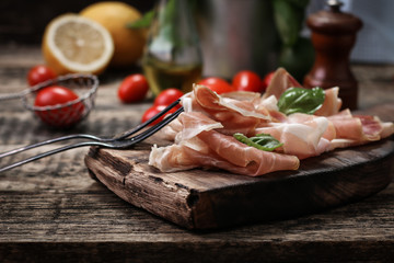 thin slices of prosciutto with mixed with basil, cherry tomatoes on wooden cutting board,vintage...