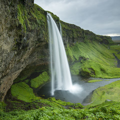 view to cave and waterfall with gray clouds in Iceland