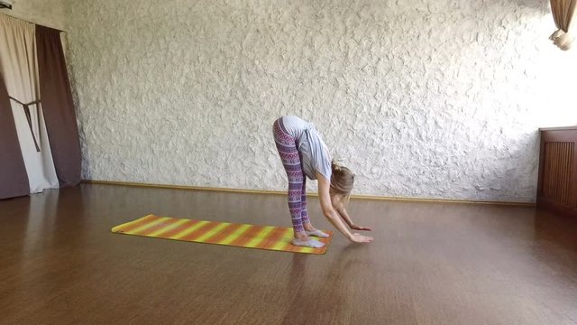 The young blonde girl practicing yoga in the hall. Asanas the greeting to the sun. Surya namaskar. 4K