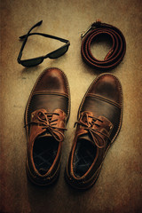 Still life with brown leather shoes, sunglasses and belt over grunge background