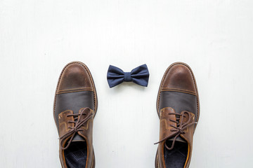 Men's accessories outfits with brown leather shoes and bow tie, top view, flat lay on wooden board background 
