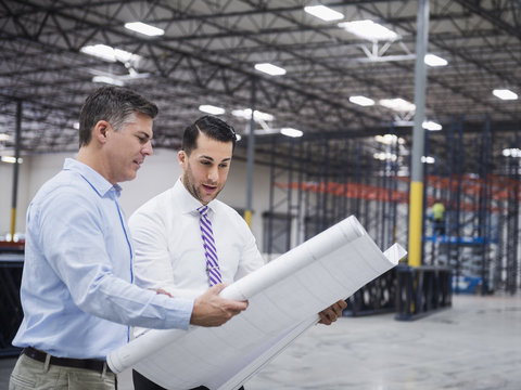 Caucasian architects reading blueprints in warehouse