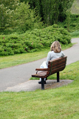 Mature female blond beauty relaxing on park bench outdoors.