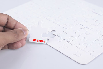 Closeup of businesspeople about to put four puzzle pieces with negative word