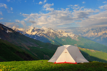 gray tent in grass on background of mountains and rocks