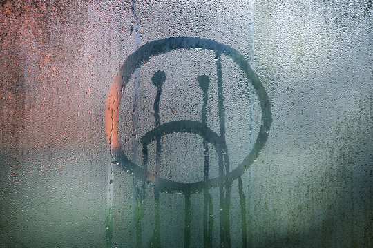 Sad upside down smiley hand drawn symbol on wet glass background.