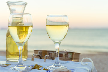 The carafe of white wine and a glass of wine on the beach, sunset, dinner by the sea, holiday, romance. Holidays in Greek wine in Greece.