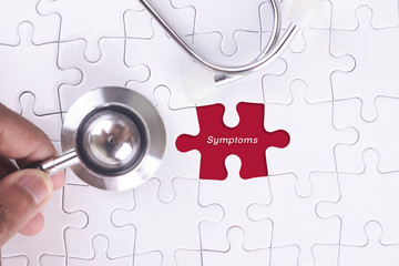 Medical Concept - A doctor holding a Stethoscope on missing puzzle with Symptoms  word