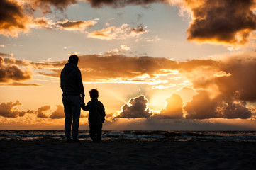 A woman holding a child's hand during sunset