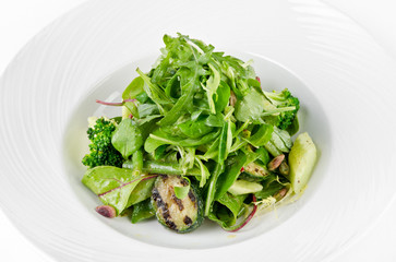 Salad of green vegetables with broccoli, zucchini and walnut dressing on a plate on a white background, closeup