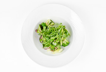 Salad of green vegetables with broccoli, zucchini and walnut dressing on a plate on a white background, top view