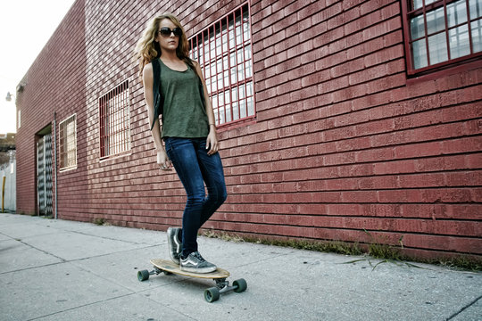 Mixed race woman riding skateboard on city street