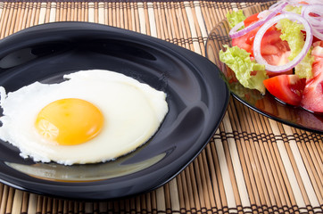 Fried eggs with yolk on a black plate and a salad