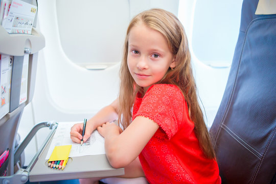 Adorable little girl traveling by an airplane. Kid drawing picture with colorful pencils sitting near aircraft window