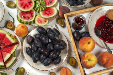 Colorful fruit set of purple, red and orange background in bowls. Plum, peaches, watermelon sliced above white tabletop
