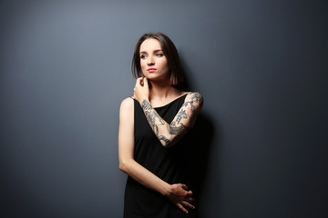 Beautiful young woman with tattoo posing on gray background