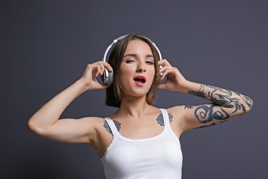 Beautiful young woman with tattoo wearing headphones and posing on gray background