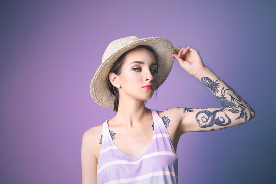 Beautiful young woman with tattoo wearing hat and posing on blue background