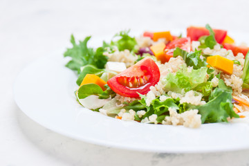Homemade autumn healthy salad with quinoa, salad leaves, tomatoes, pumpkin and feta cheese on a white plate, closeup, selective focus