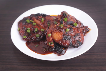 Grilled chicken or ayam golek on white plate, wooden background.