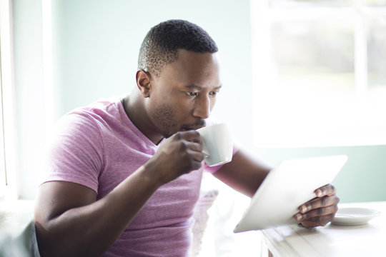 Black man drinking coffee using digital tablet