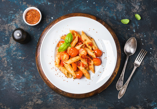 Pasta penne with tomato sauce, fresh basil and roasted tomatoes. Old painted dark plywood background, top view, horizontal composition