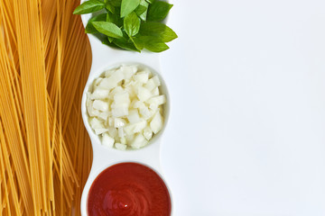 Basil, sliced onions and tomato paste in white bowl with raw spaghetti scattered around on white background. Concept image for Italian cuisine. Top view with plenty of copy space