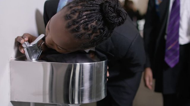  Young Girl Takes A Drink From Water Fountain In School Corridor.